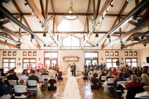 Wedding ceremony in an elegant indoor venue with exposed wooden beams and a flower-lined aisle.