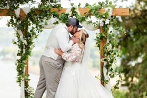 Couple shares a romantic kiss under a greenery-adorned wooden arch during their wedding ceremony.