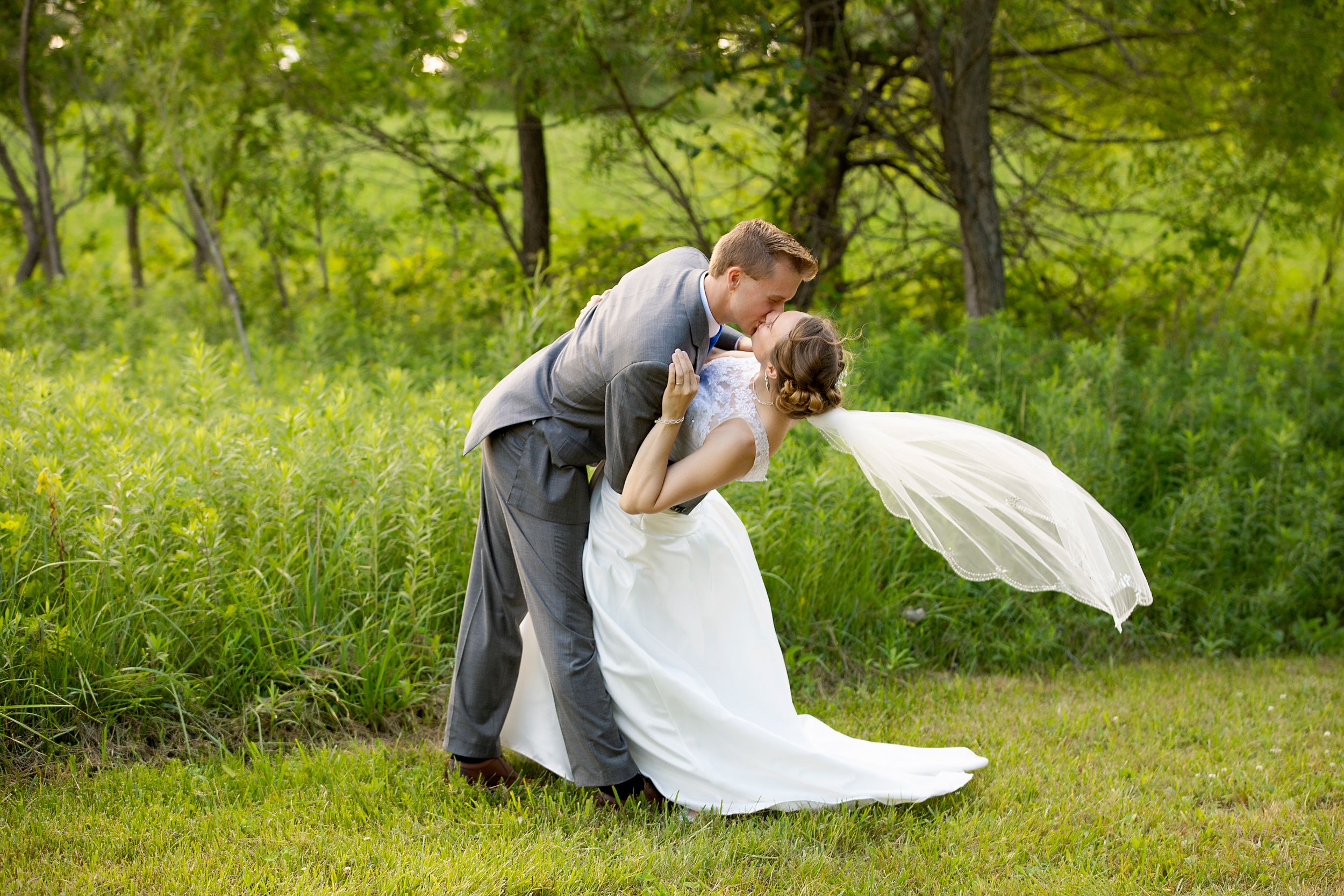 A romantic dip pose captured during wedding portraits in a green garden.
