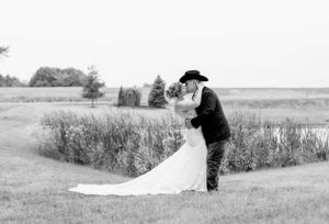 Black and white portrait of wedding couple embracing in rustic field setting.