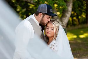 Intimate wedding portrait outdoors with soft natural lighting and trees in background.