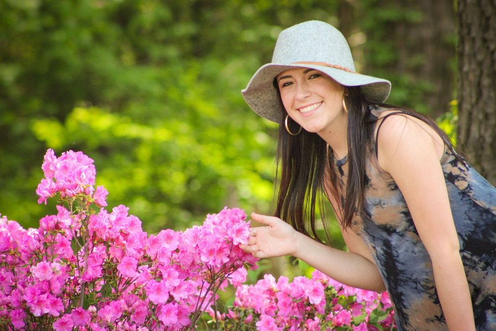 A woman in a dark top poses near vibrant pink azalea bushes in a garden setting.