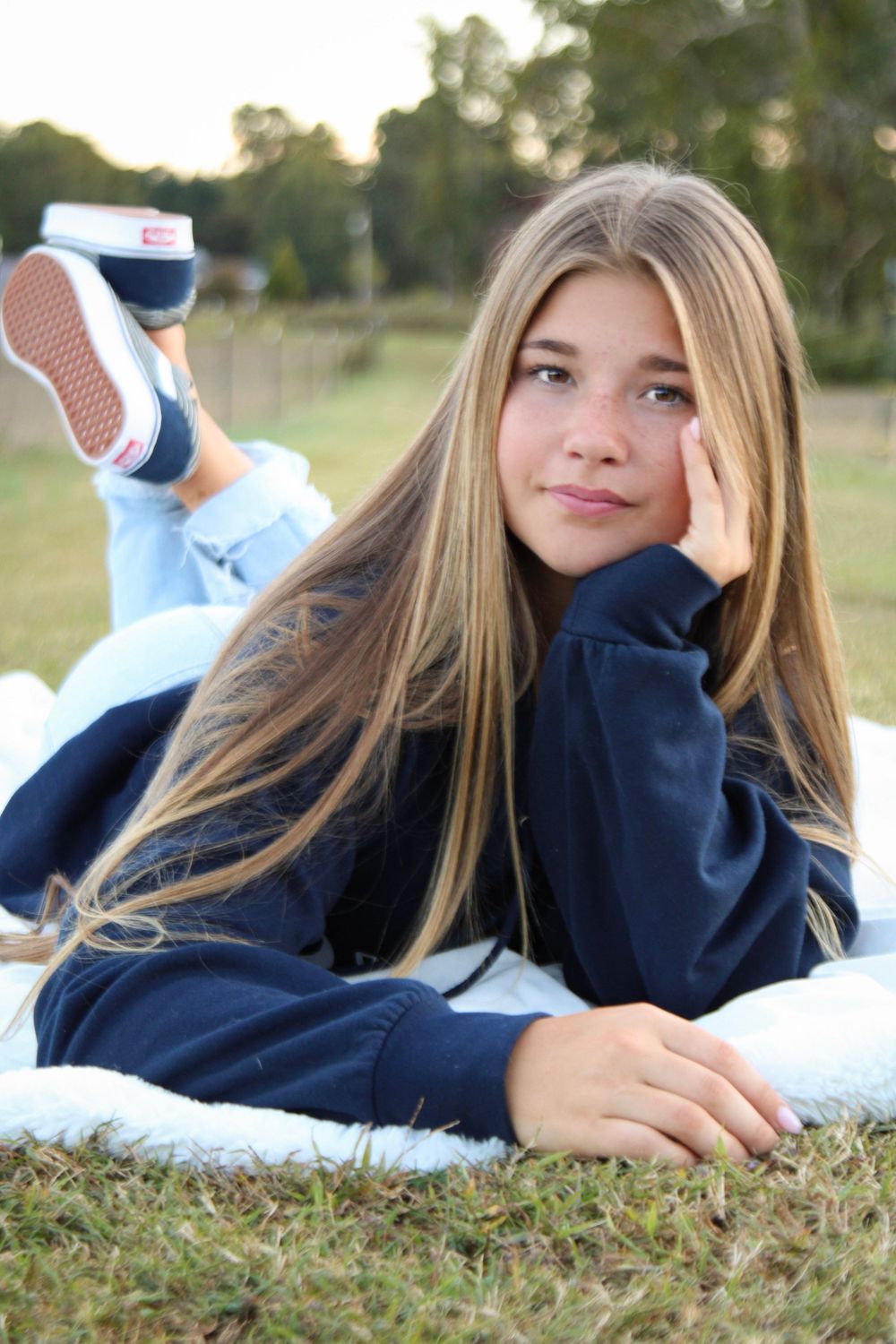 Casual outdoor portrait lying on grass wearing navy sweater and jeans.