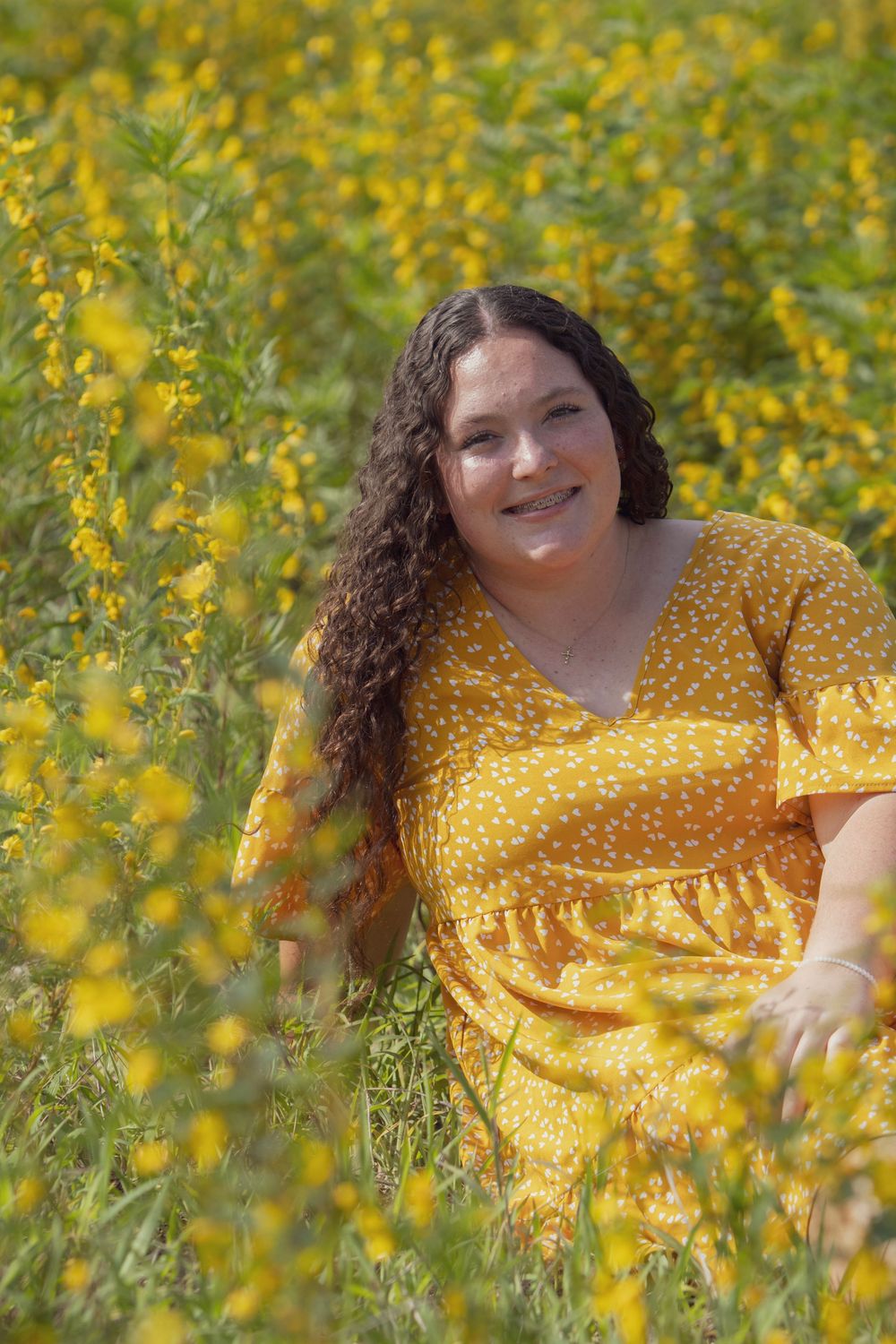 A bright yellow dress complements the surrounding field of golden wildflowers in a sunny outdoor portrait.