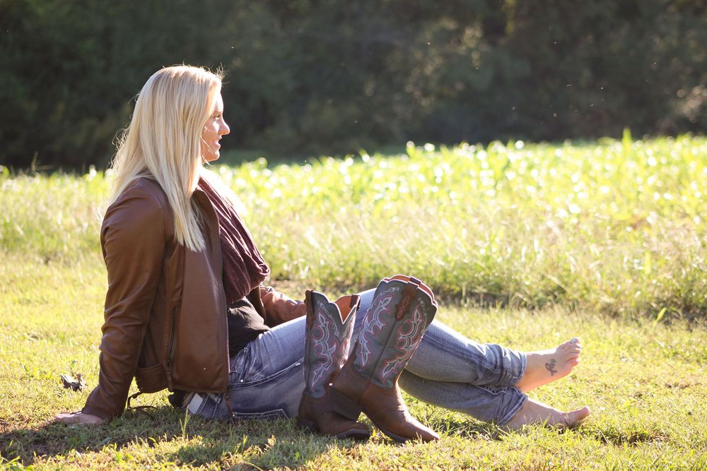 Someone relaxes on grass wearing boots and casual attire in golden sunlight.