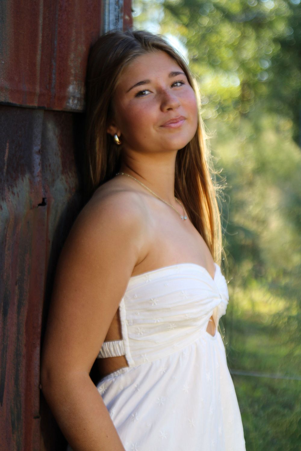 Outdoor portrait by a rustic red wall in a white sundress.