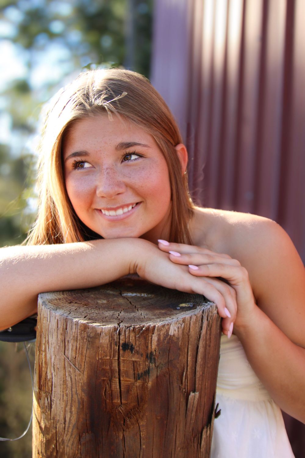 Natural lighting portrait leaning on wooden post in white dress.