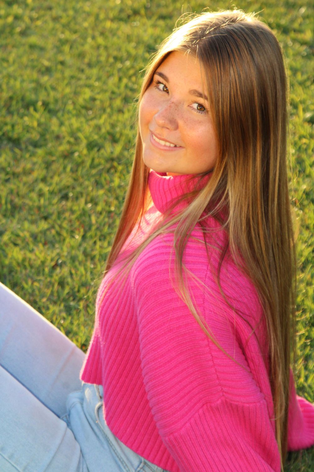 Person in vibrant pink sweater relaxing on sunny grass with artistic poses.