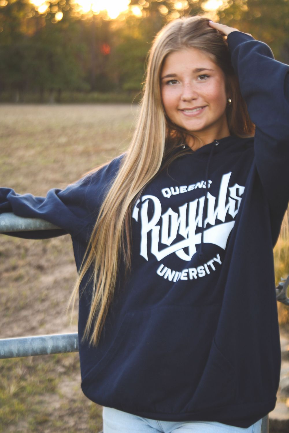 Person in navy university sweatshirt posing outdoors at sunset.