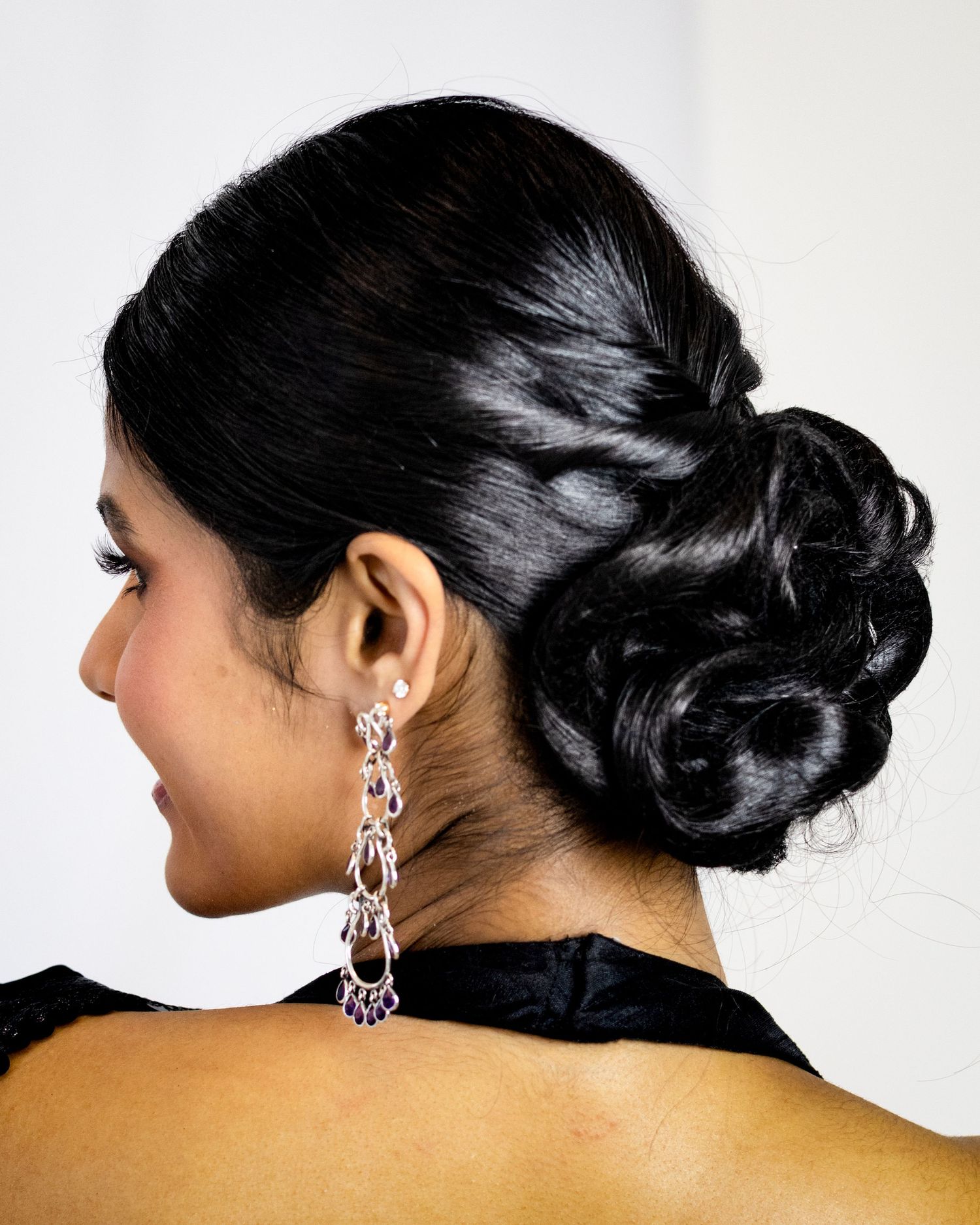Elegant updo hairstyle with curled bun and dangling crystal earring shown from behind.
