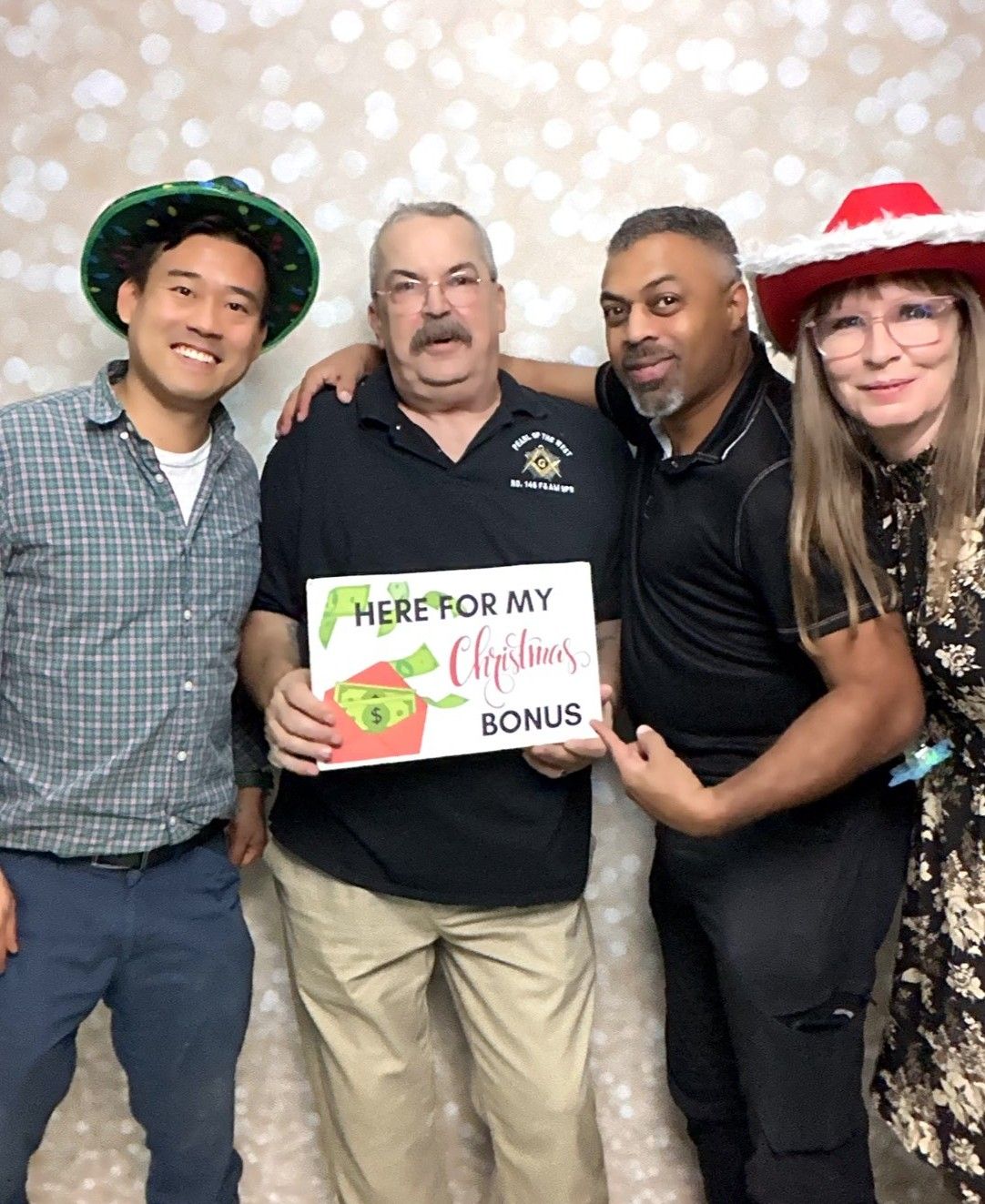 A diverse group poses together holding a Christmas bonus sign against a sparkly backdrop.