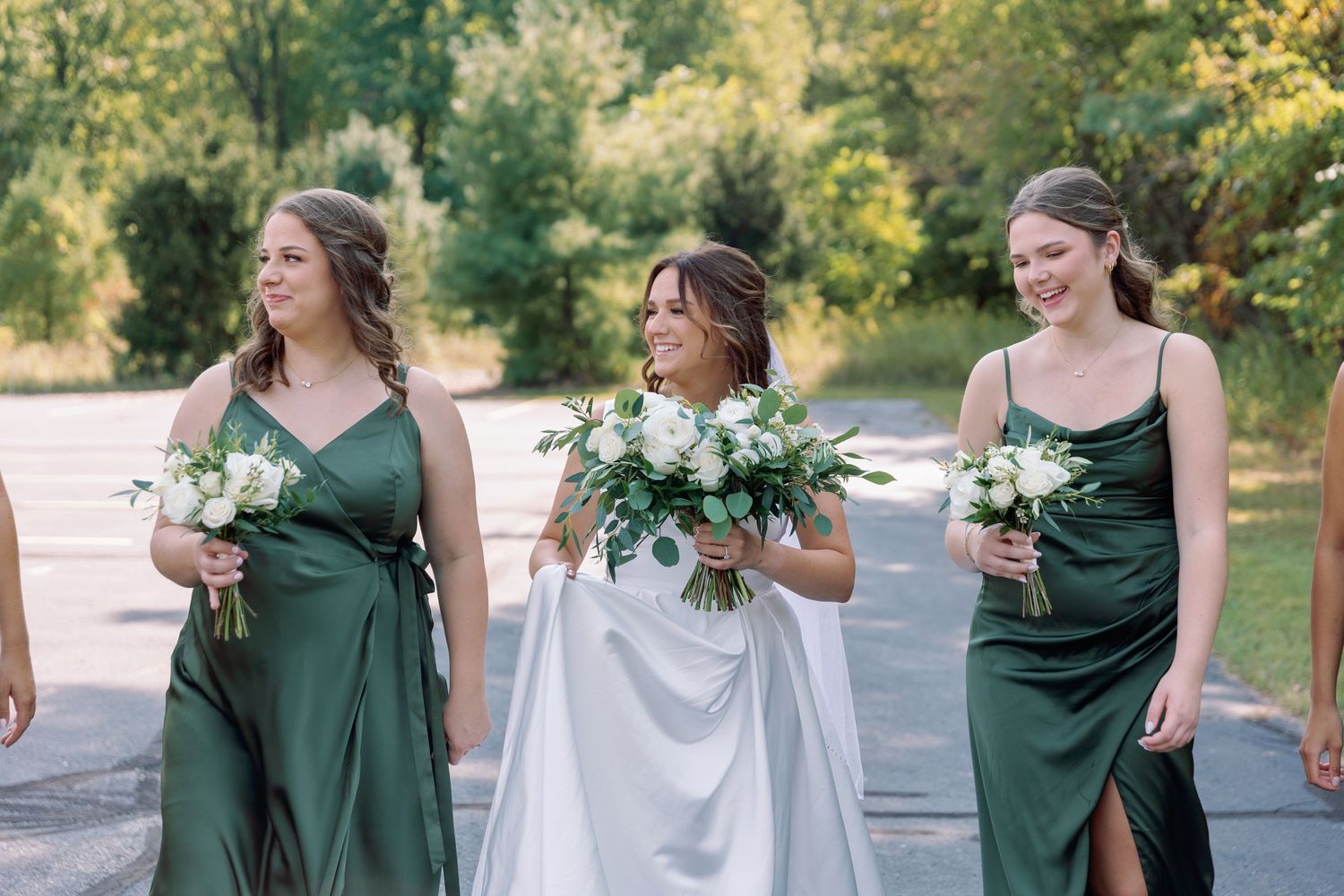 Bridesmaid in an outdoor wedding party walk together holding white floral bouquets in green and white dresses in Grand Rapids.