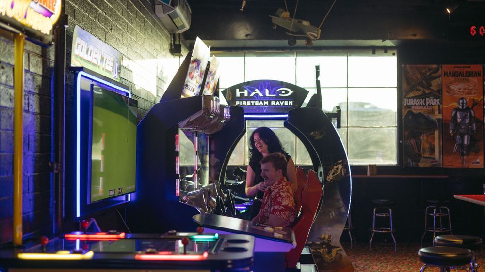 Two gamers enjoying the Halo arcade setup in a dimly lit gaming room with neon lighting and branded decor.