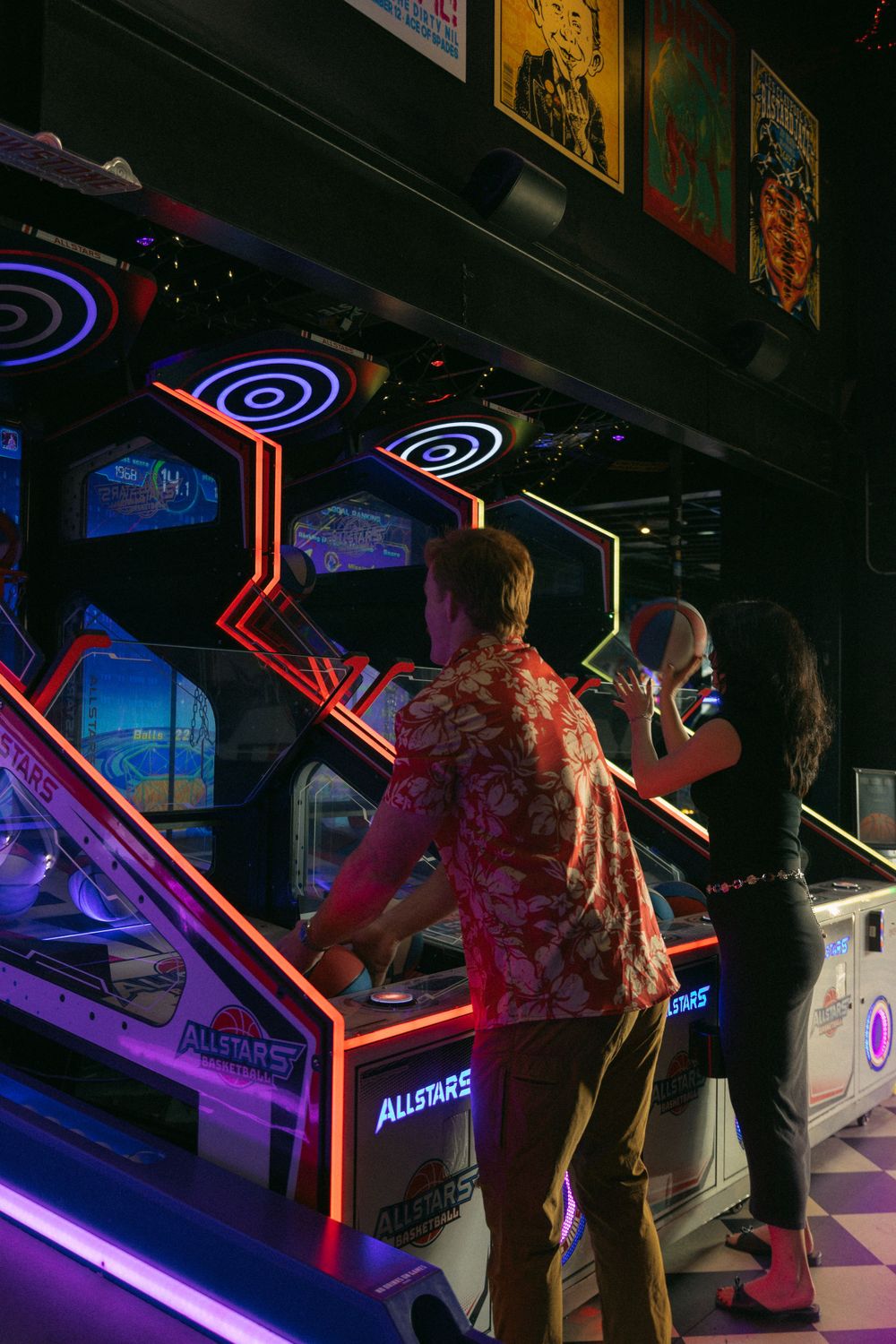 People enjoying colorful arcade games with neon lights glowing in a dark gaming arcade at night.