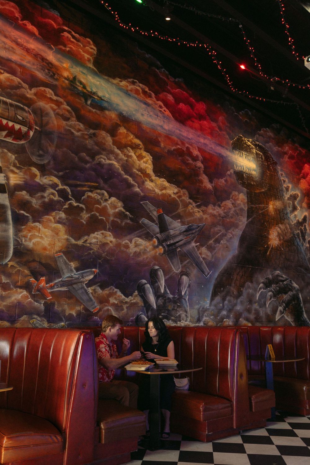 A retro diner interior featuring red leather booths and a dramatic cosmic-themed mural with colorful clouds on the ceiling.