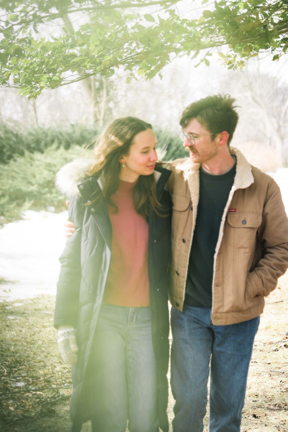 A couple takes a romantic stroll along a misty tree-lined path on a dreamy sun-drenched afternoon.