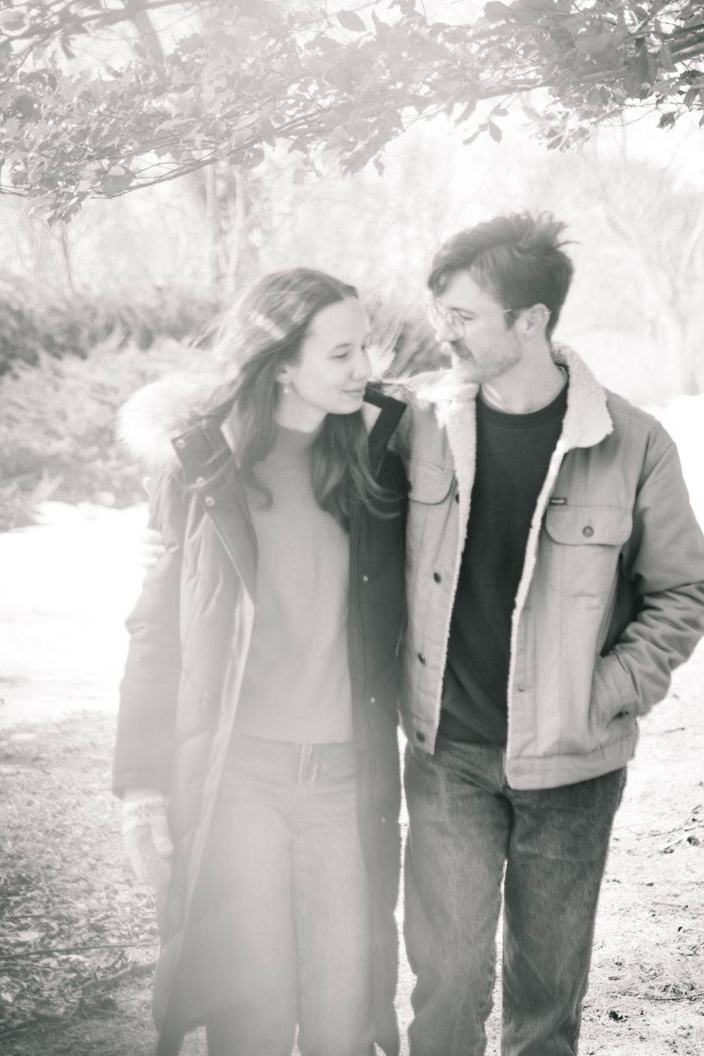 A romantic black and white photo of a couple sharing a tender moment while walking outdoors on a misty path.