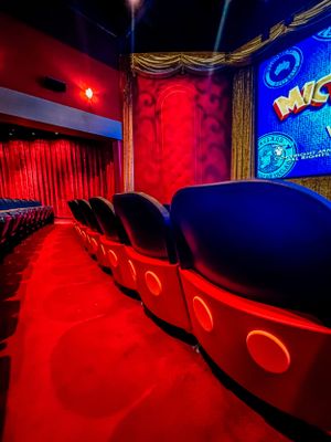 A movie theater auditorium with dramatic red lighting and rows of empty seats creates an atmospheric cinematic ambiance.