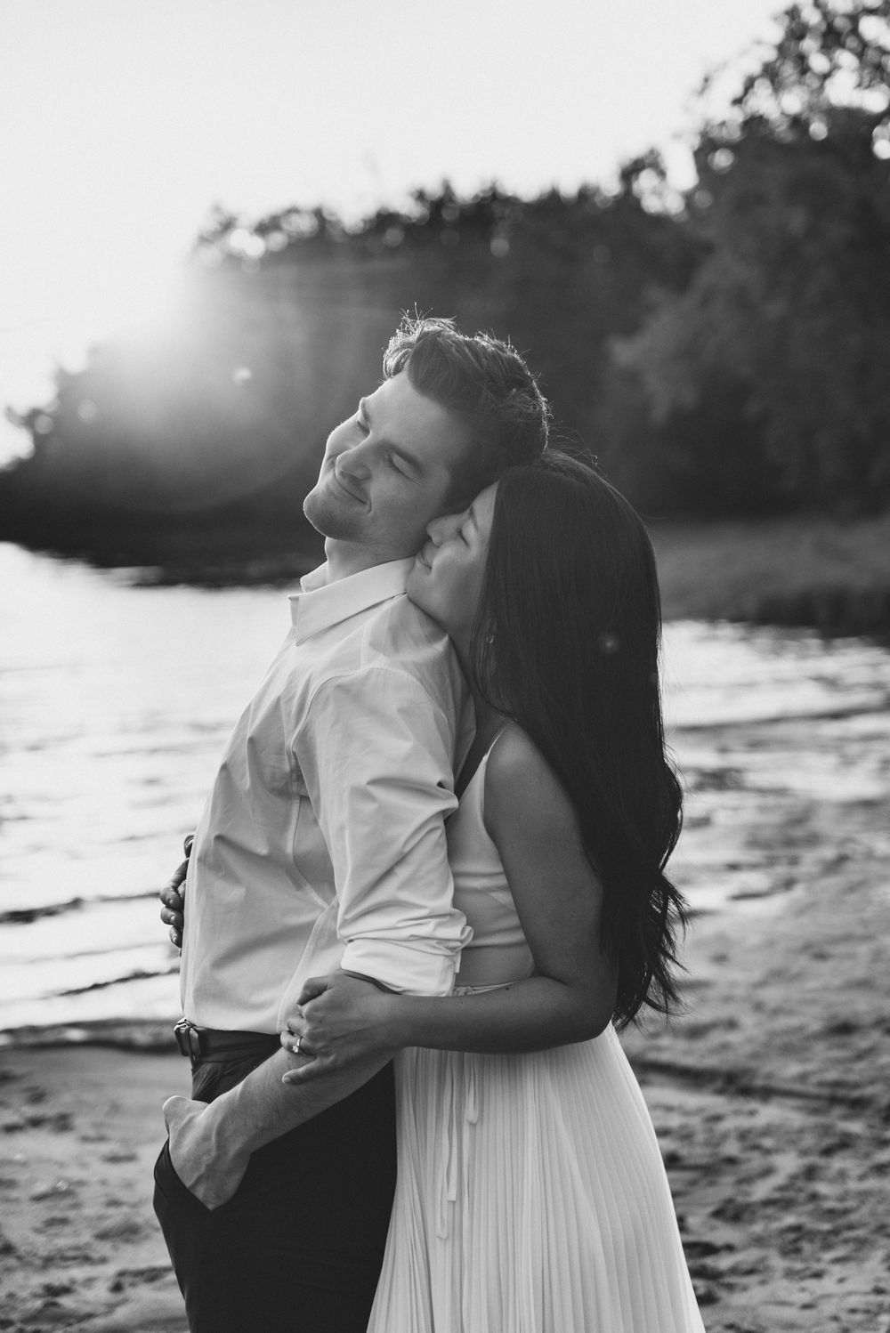 A romantic couple embraces on a beach at sunset in black and white, creating a dreamy silhouetted effect.