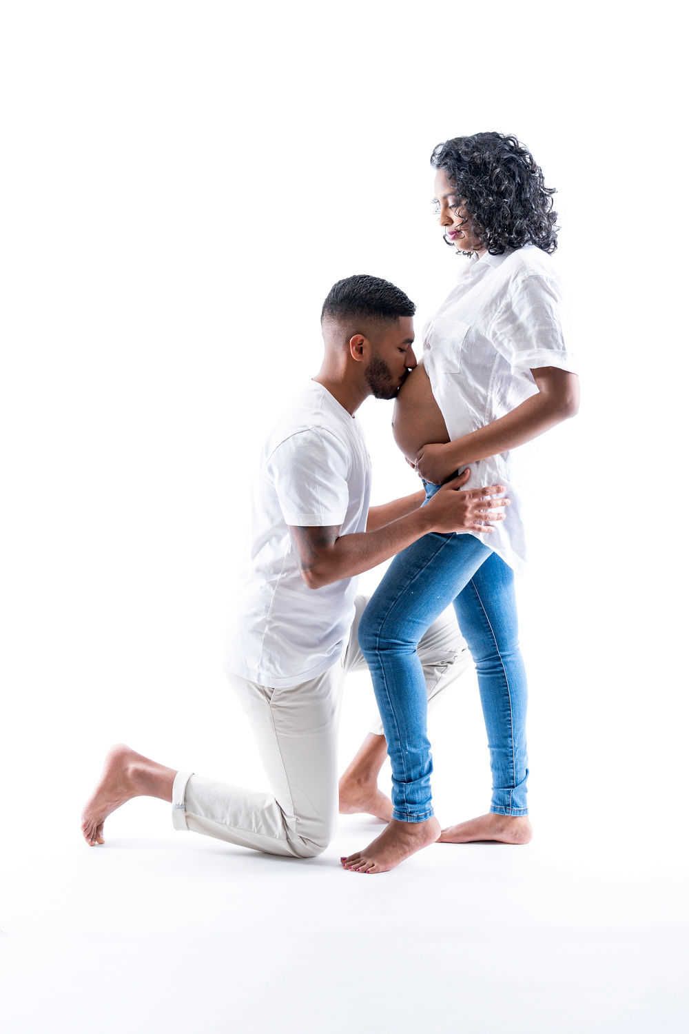A couple dressed in white and denim pose together against a white background, with one person kneeling.