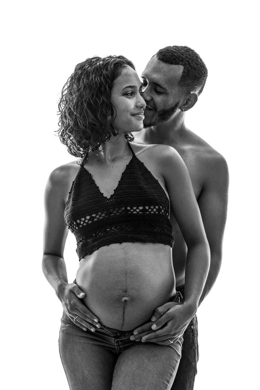 A black and white maternity photo shows an intimate moment between a couple as they embrace the pregnant belly.