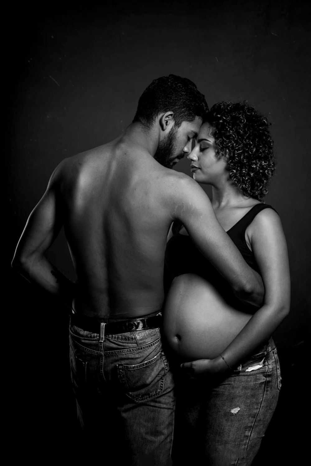 Black and white artistic pregnancy photo of intimate couple embracing, highlighting pregnant belly.