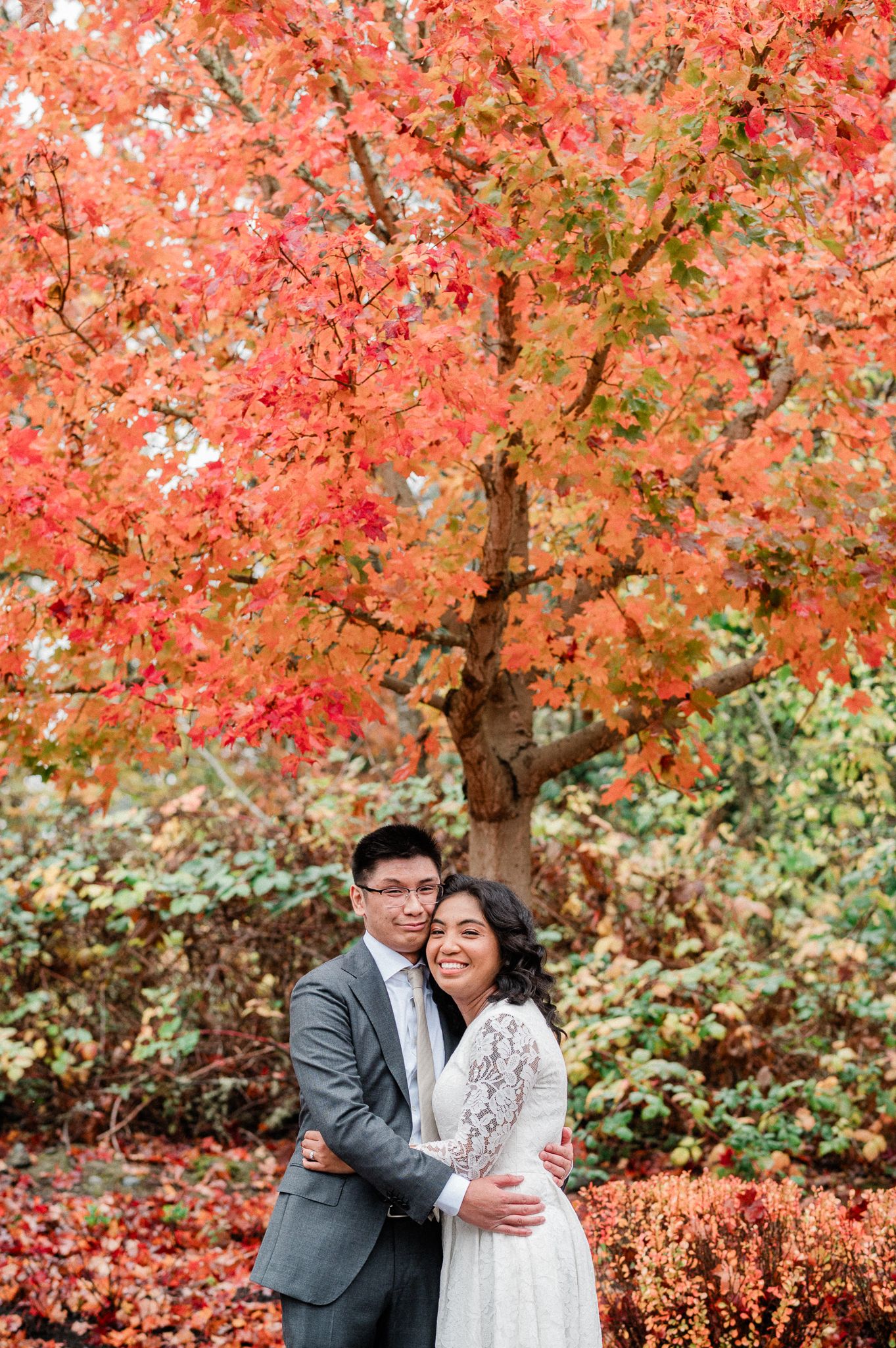 A couple shares a joyful moment together against a backdrop of vibrant autumn foliage with red maple leaves.