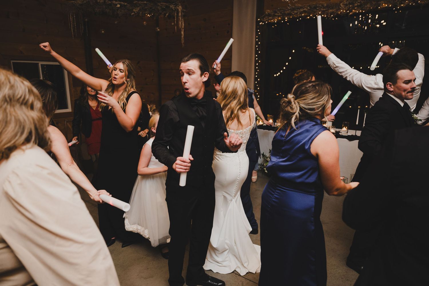 Wedding guests dance and celebrate on a dimly lit dance floor during an evening reception celebration.