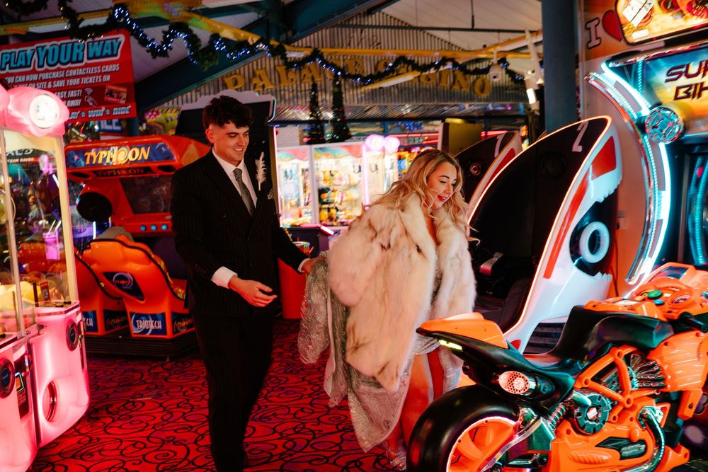 Bride and groom preparing to climb onto motorbike game in Weymouth arcade during their New Year’s Eve wedding