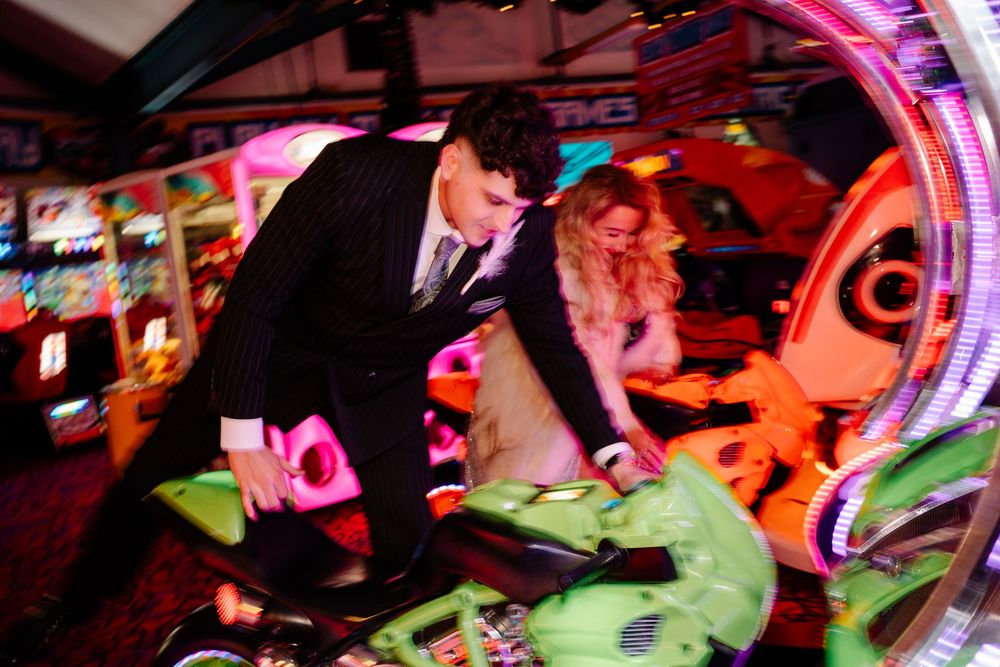 Bride and groom climbing onto motorbike game in Weymouth arcade during their New Year’s Eve wedding