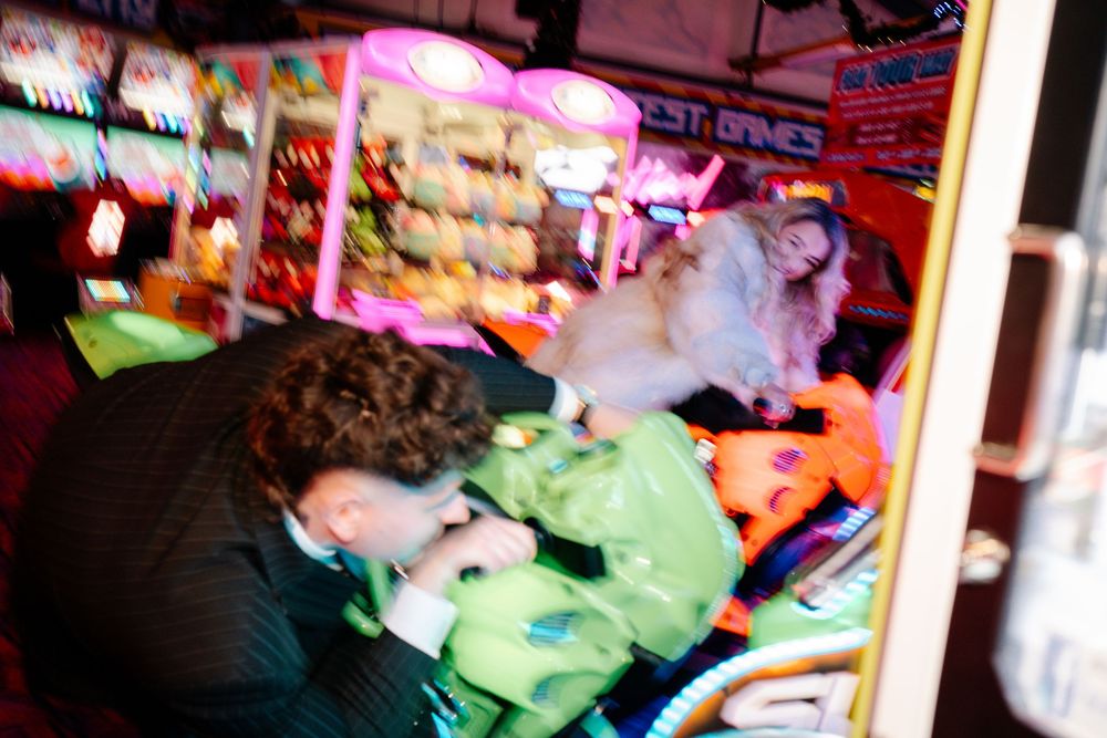 Bride and groom playing together in Weymouth arcade during their New Year’s Eve wedding on kids motorbike game