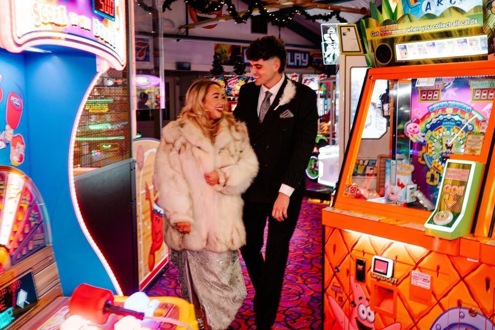 Bride and groom walking together in Weymouth arcade during their New Year’s Eve wedding surrounded by lights and games