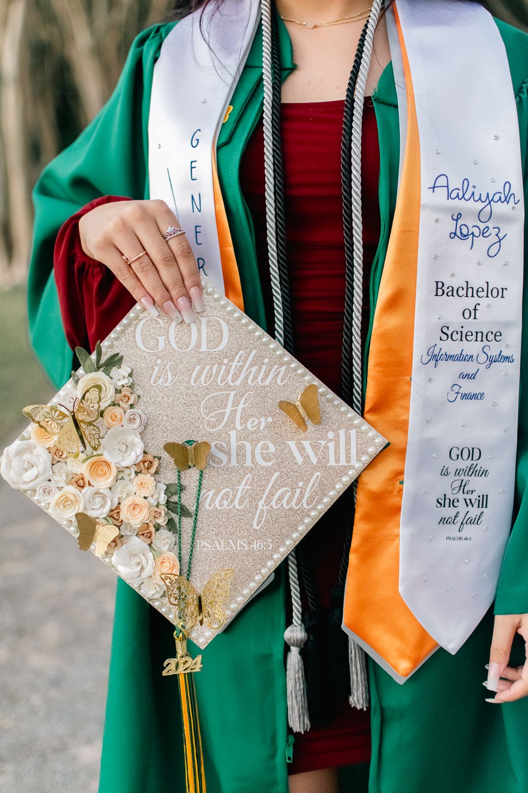 A graduation photo showing green regalia and decorated cap with religious messaging.