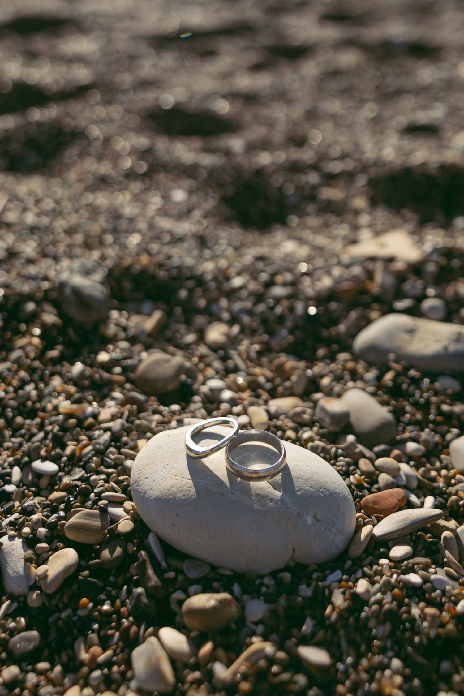Wedding rings nestled among small white pebbles and stones on a beach, creating a romantic macro photograph.