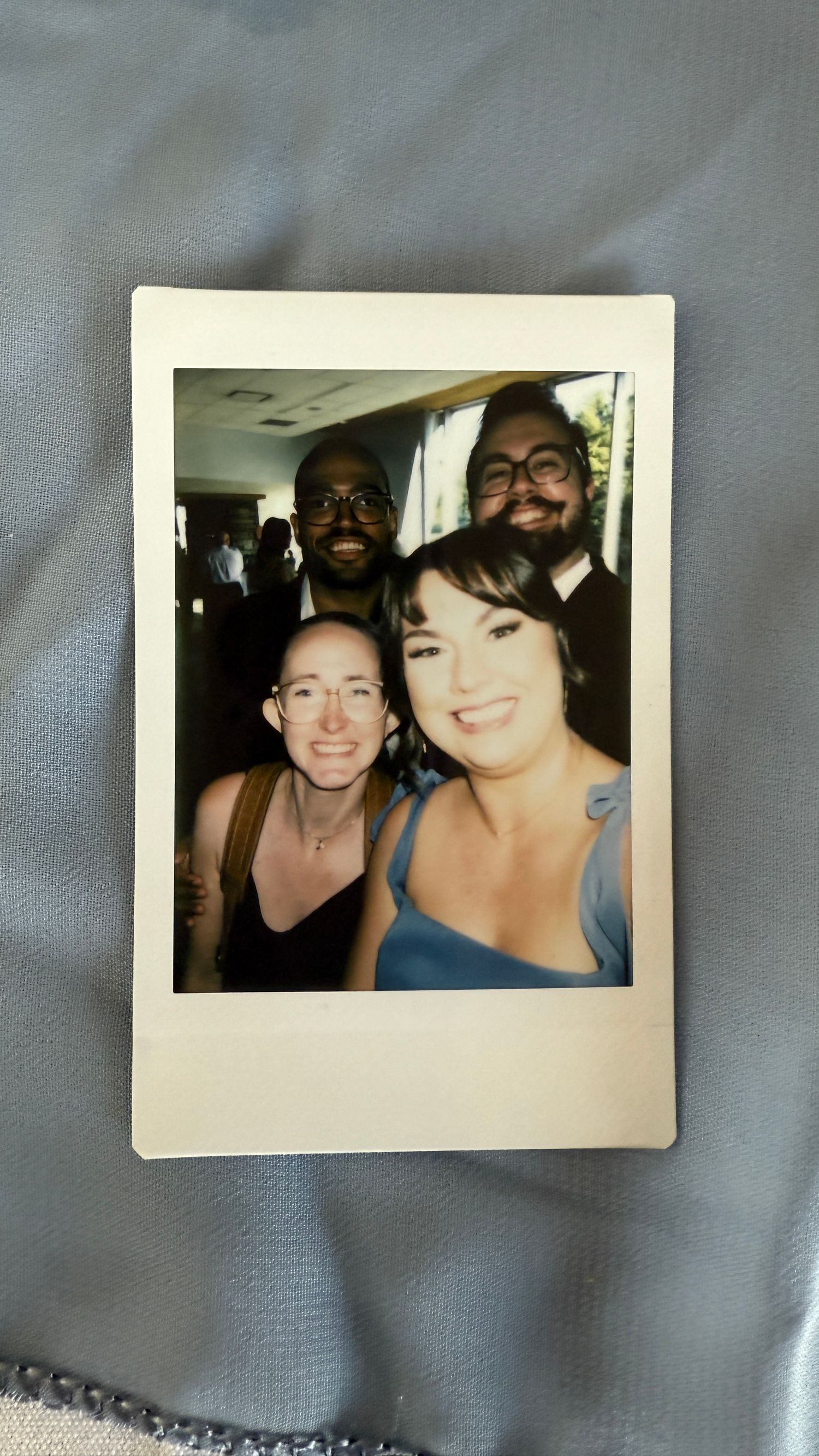 Four vintage polaroid photos arranged on a gray fabric background show friends smiling together at social gatherings.