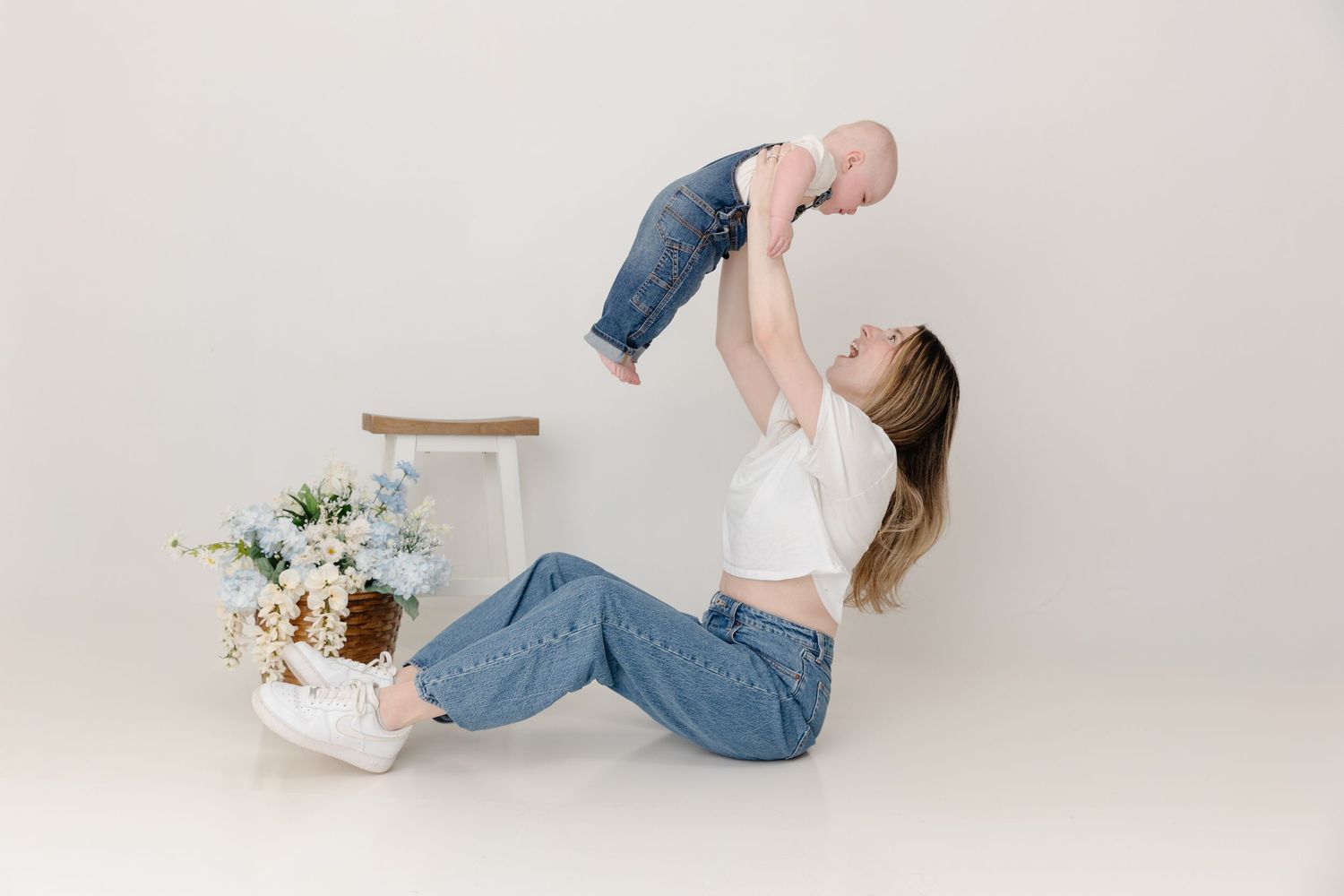 A person in jeans lies on a white background with a delicate floral arrangement in a white vase.