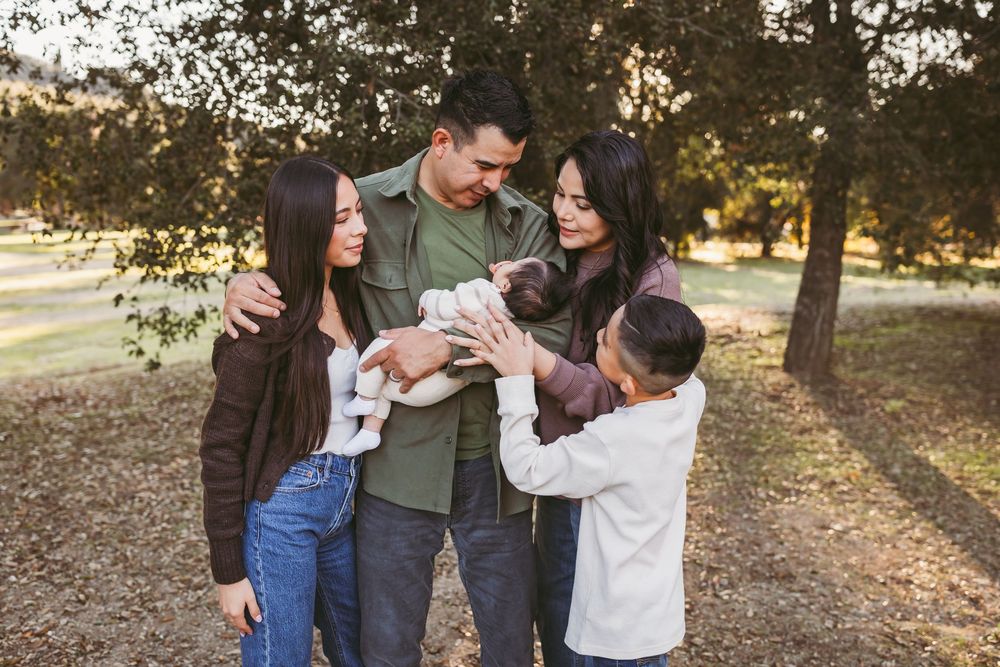 A family shares a tender moment together outdoors in a park during golden hour.