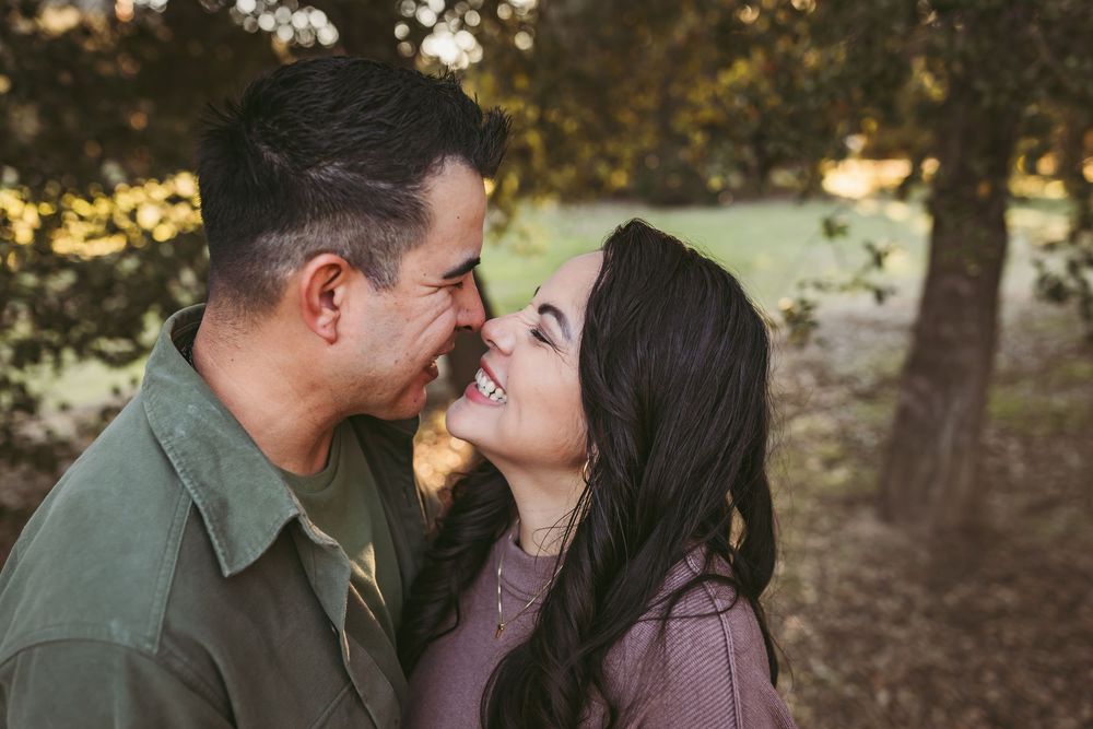 A couple shares an intimate moment while standing together in a wooded outdoor setting.