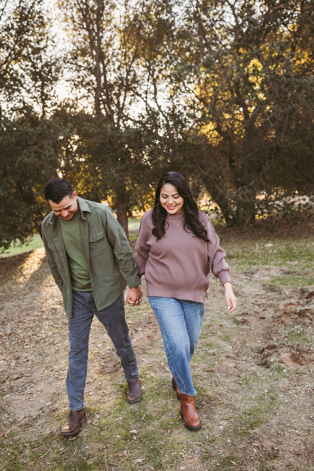 A couple walking hand in hand on a nature trail during autumn sunset wearing casual sweaters and jeans.