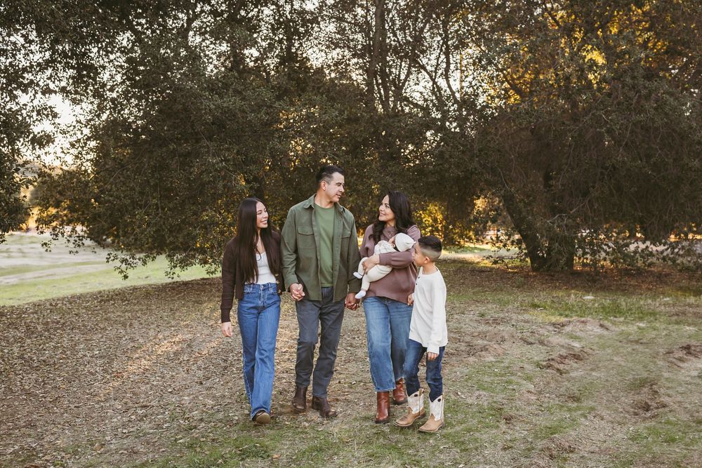 A family in casual attire poses together outdoors during an autumn photoshoot with golden sunlight filtering through trees.