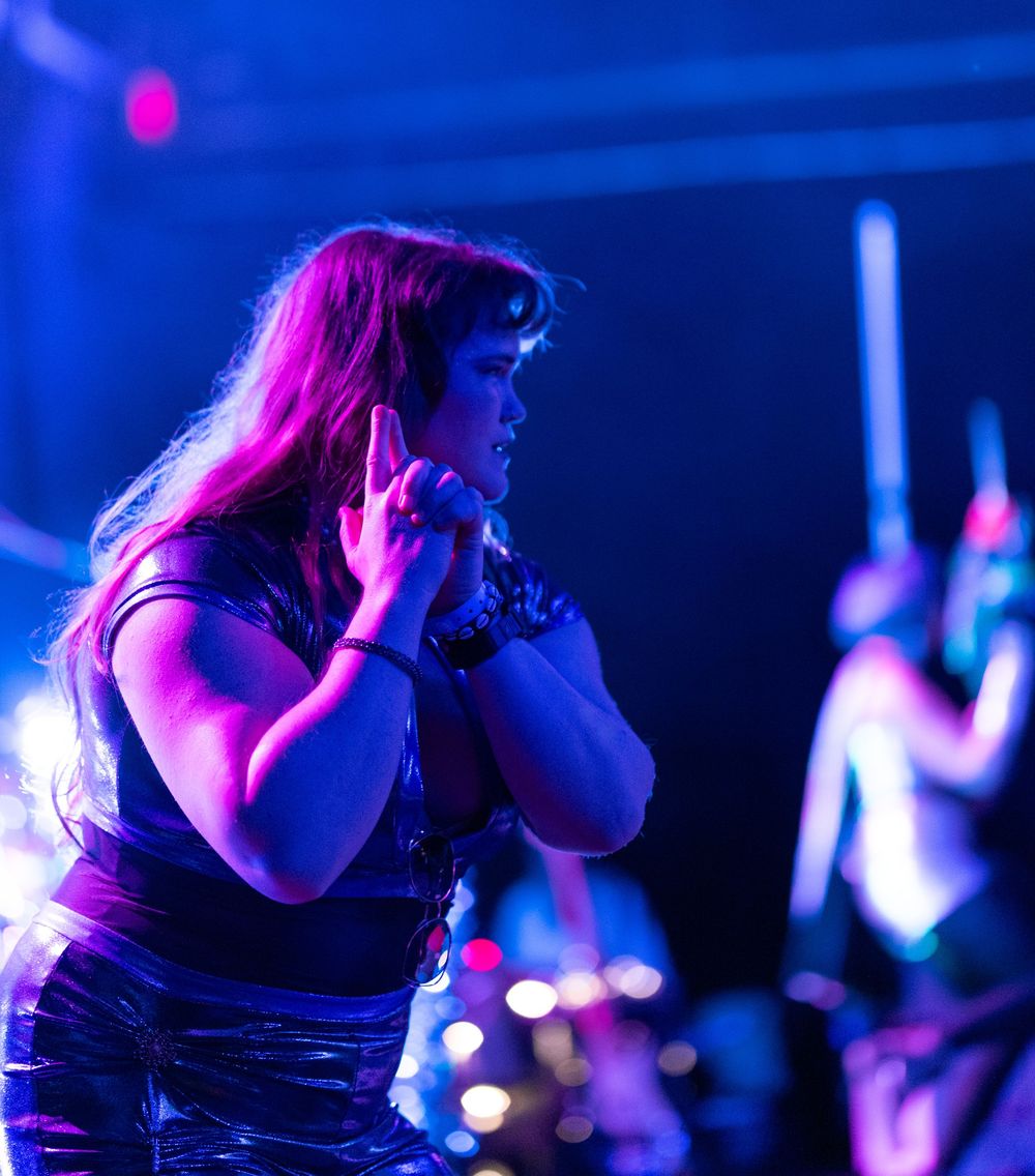 Female vocalist with long red hair performs passionately on stage under vibrant blue and purple concert lighting.