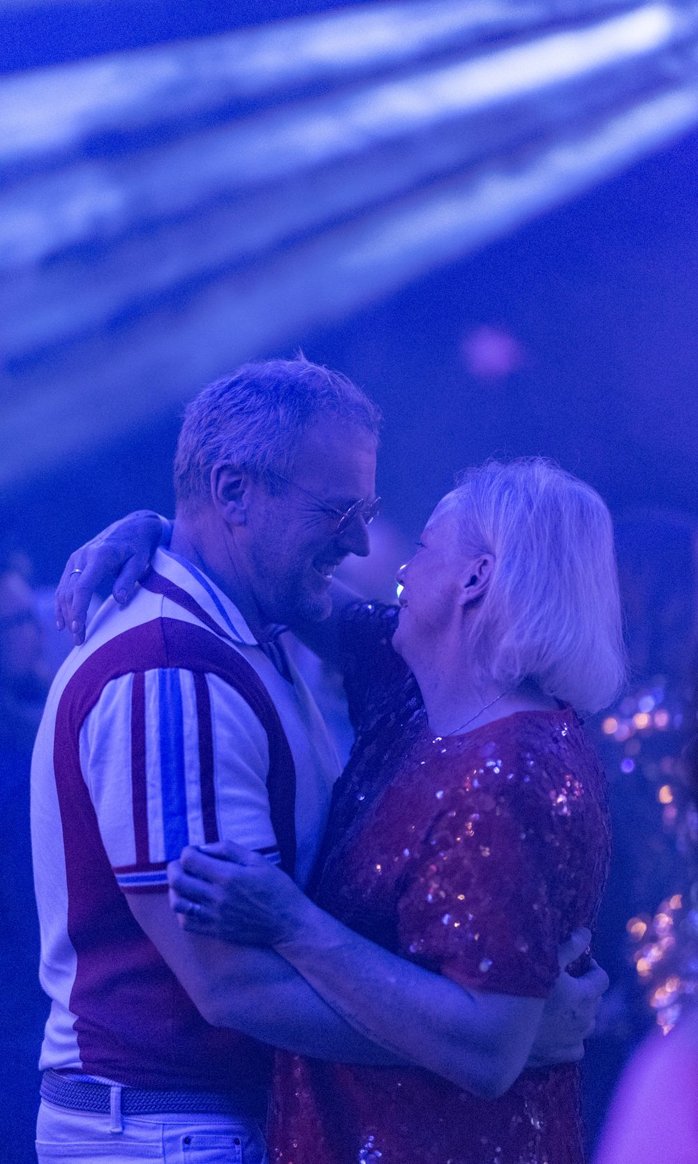 Older couple slow dancing and smiling together under blue stage lighting at a live music event.