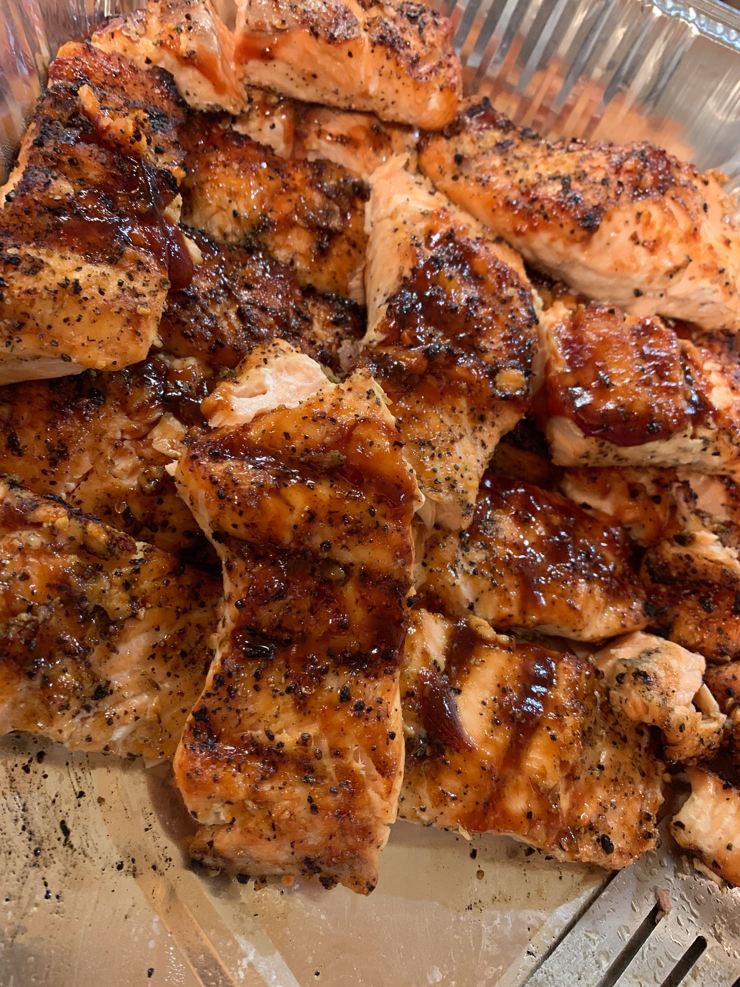 Grilled chicken pieces with charred seasoning and spices on a metal surface.