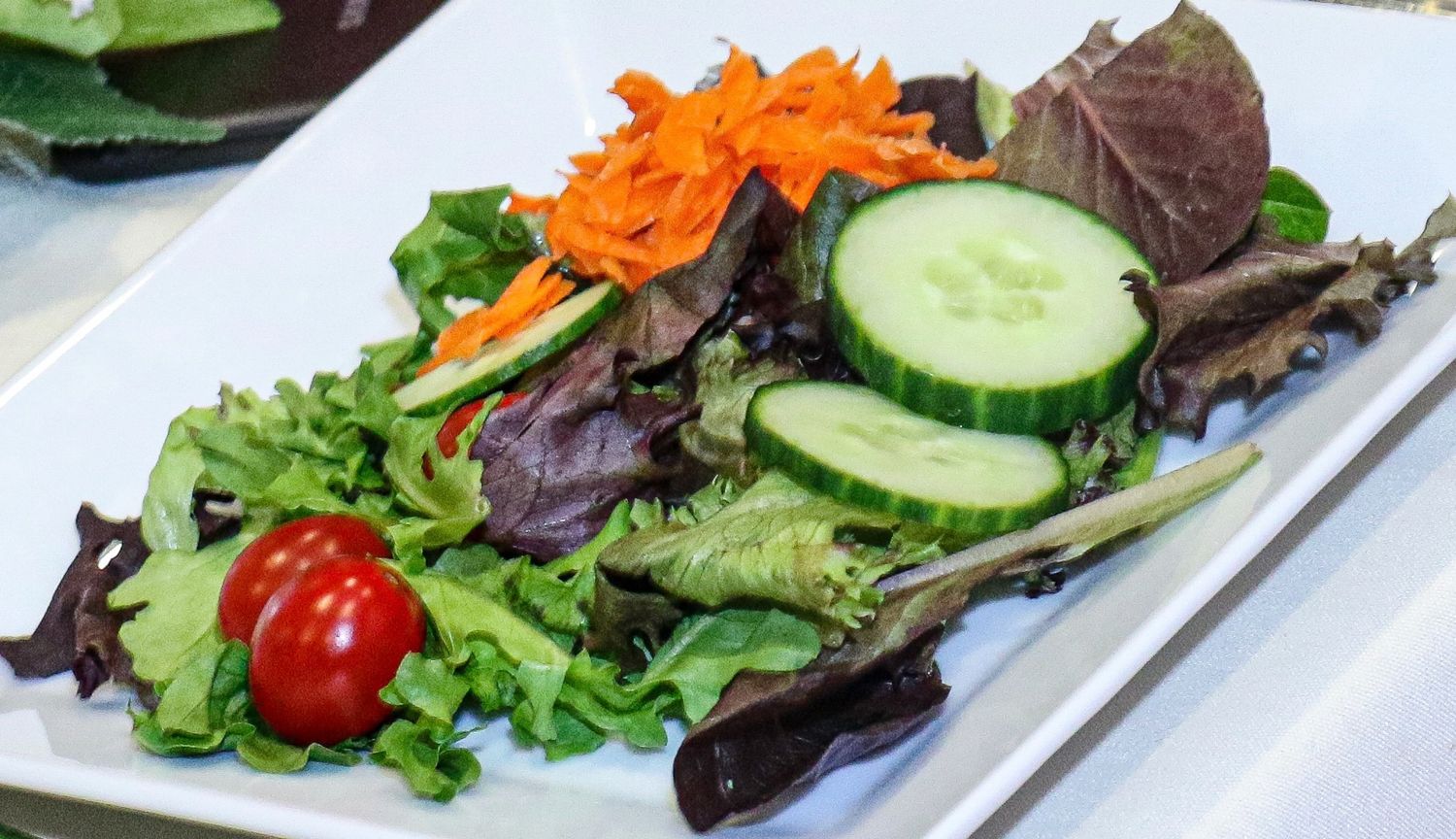 Fresh garden salad with shredded carrots, sliced cucumbers, mixed greens, and cherry tomatoes on a white plate.