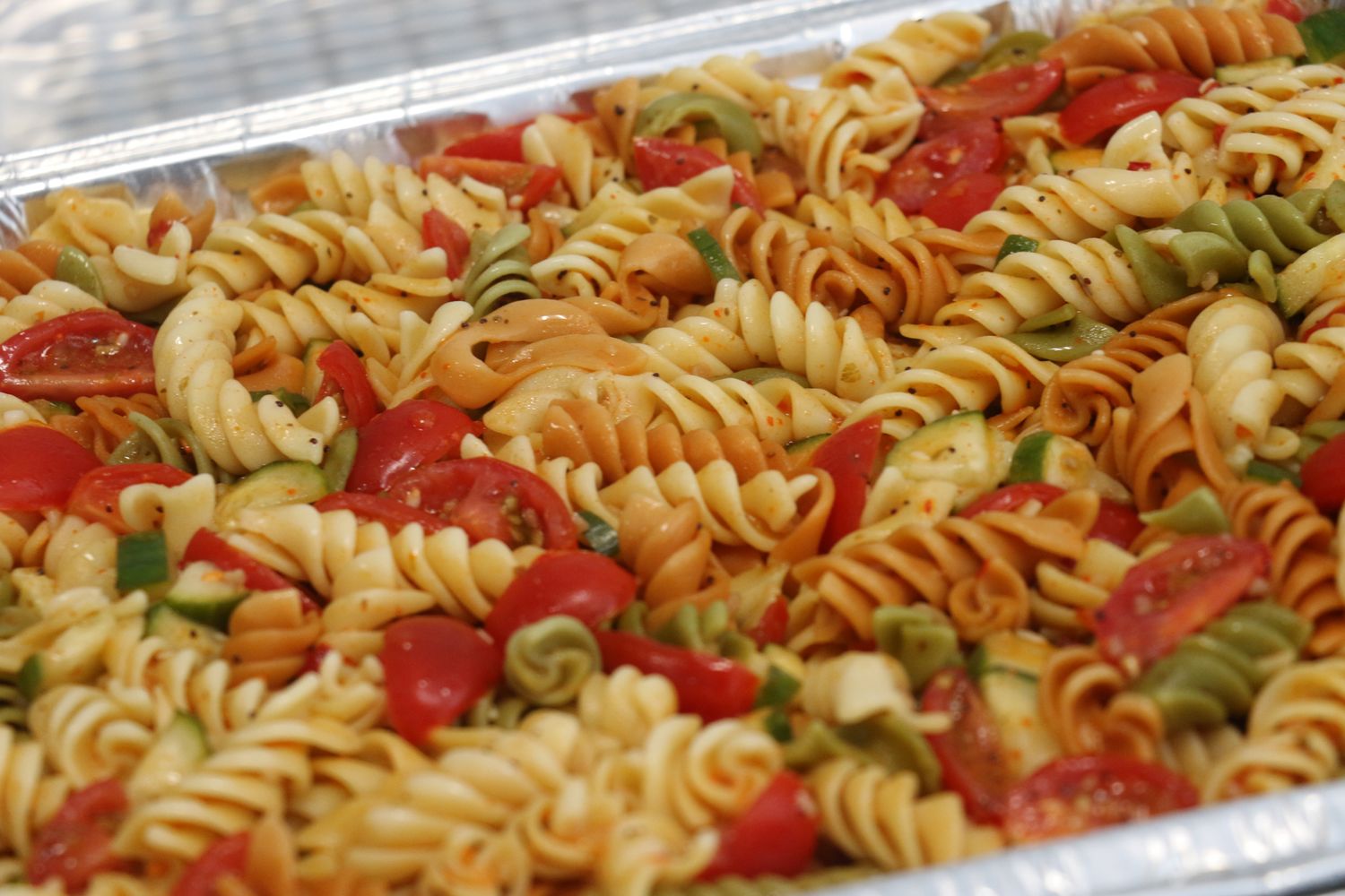 A colorful pasta salad with rotini noodles, cherry tomatoes, and fresh herbs in a clear serving dish.