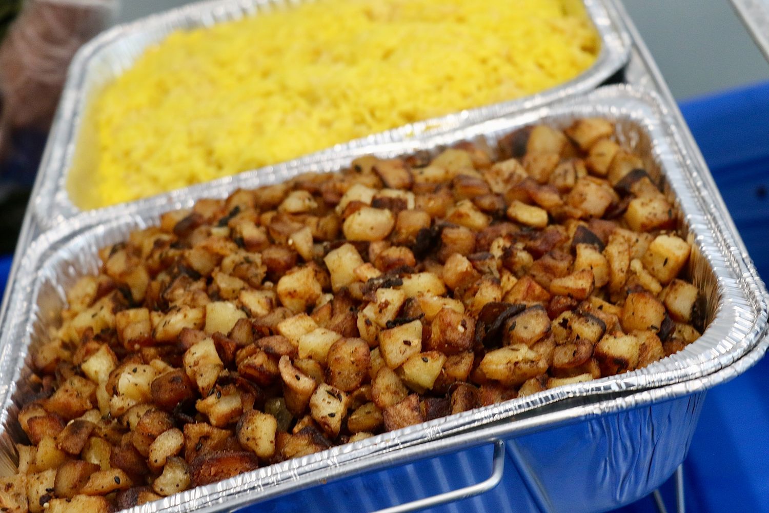 Aluminum foil containers filled with yellow rice and golden brown chicken pieces arranged in a row.
