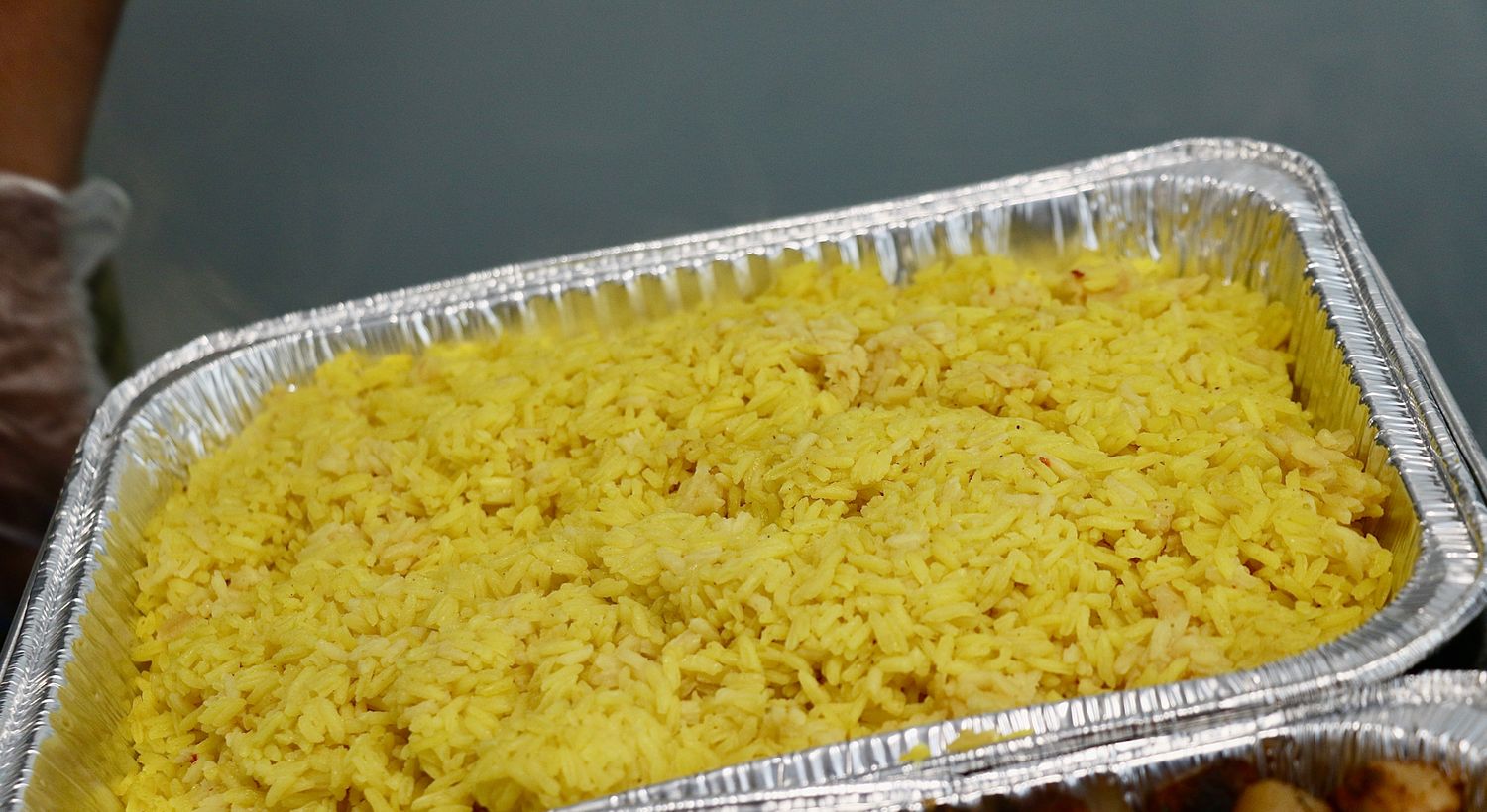 A series of aluminum foil pans filled with cooked yellow rice showing different stages of preparation.