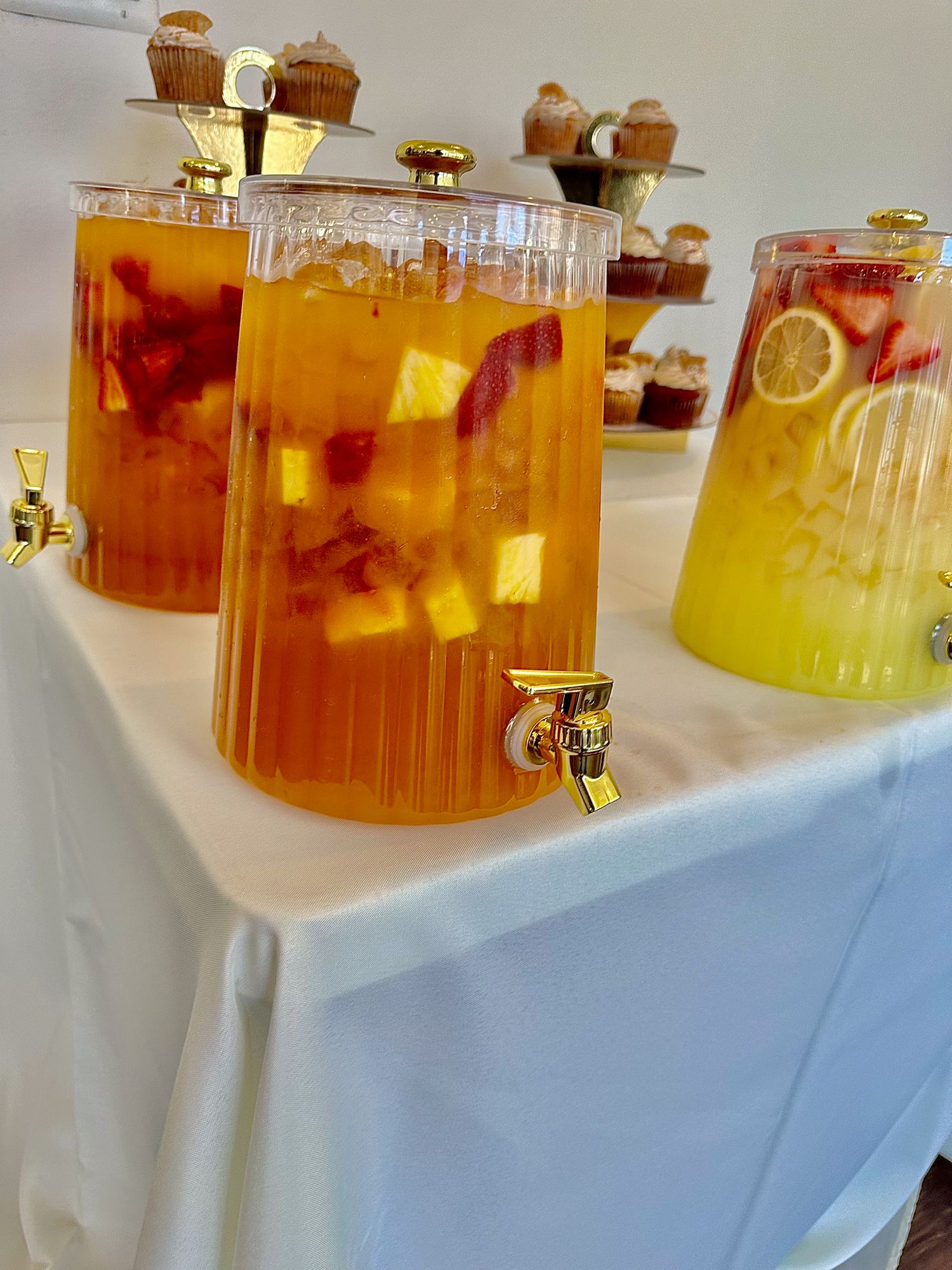 Glass beverage dispensers filled with golden and amber-colored drinks on a white tablecloth.