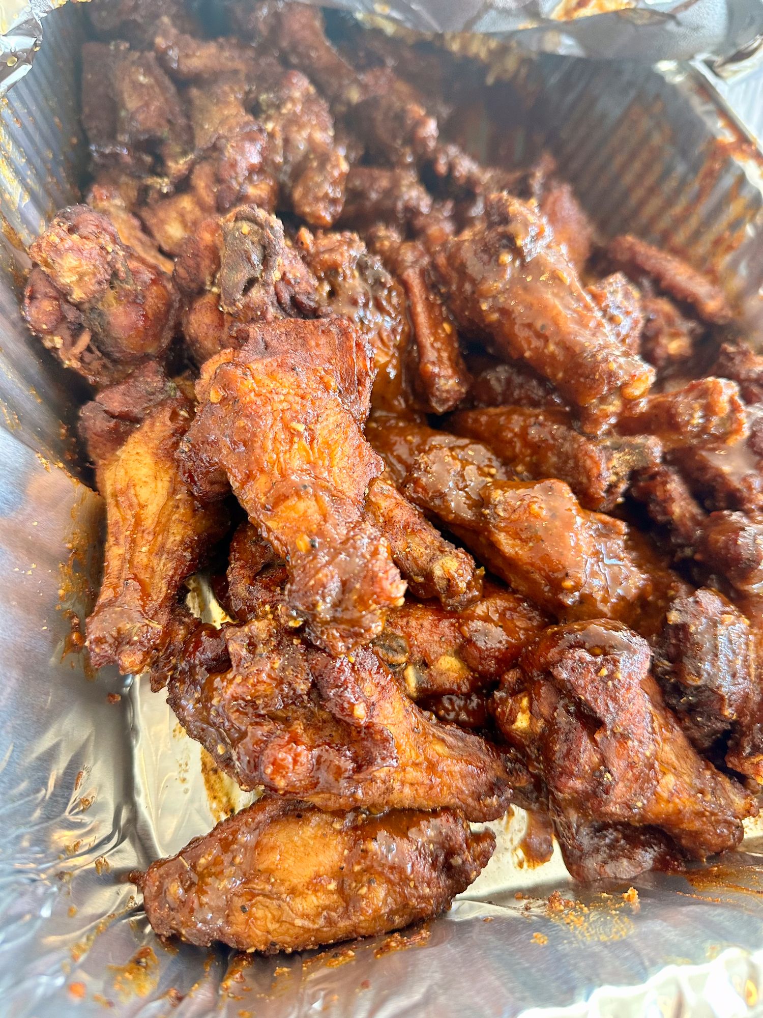 Crispy fried chicken wings coated in a spicy reddish-brown sauce served in a foil container.