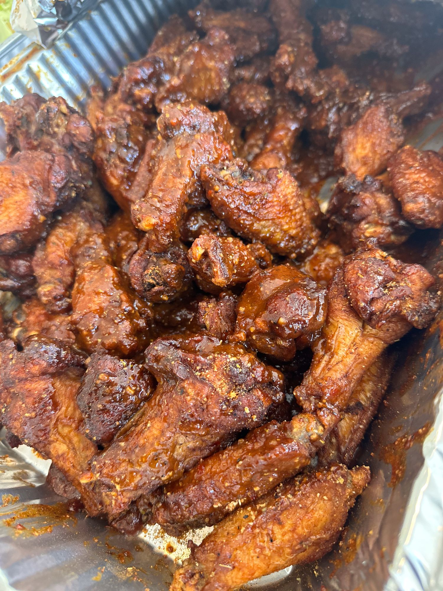 Glazed chicken wings with a dark, sticky sauce arranged in a takeout container.